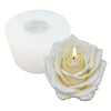 A white silicone mold for candles shown behind a finished white rose-shaped candle with a lit wick, on a plain white background.